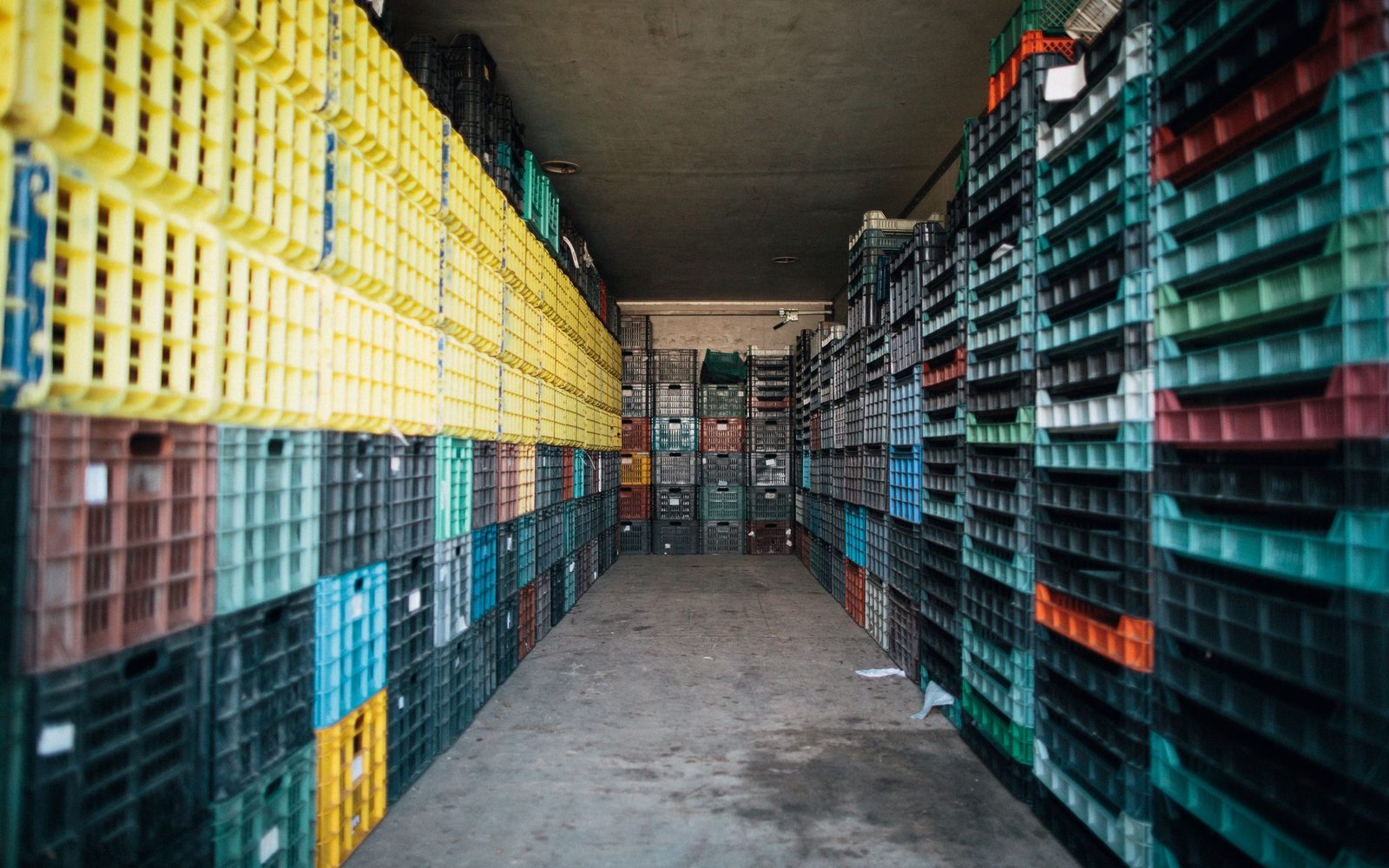 Gang in een opslaghal met tot aan het plafond gestapelde kunststof fustkisten aan weerszijden en een betonvloer